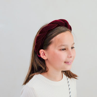Young girl wearing a burgundy velvet twist headband against a plain background