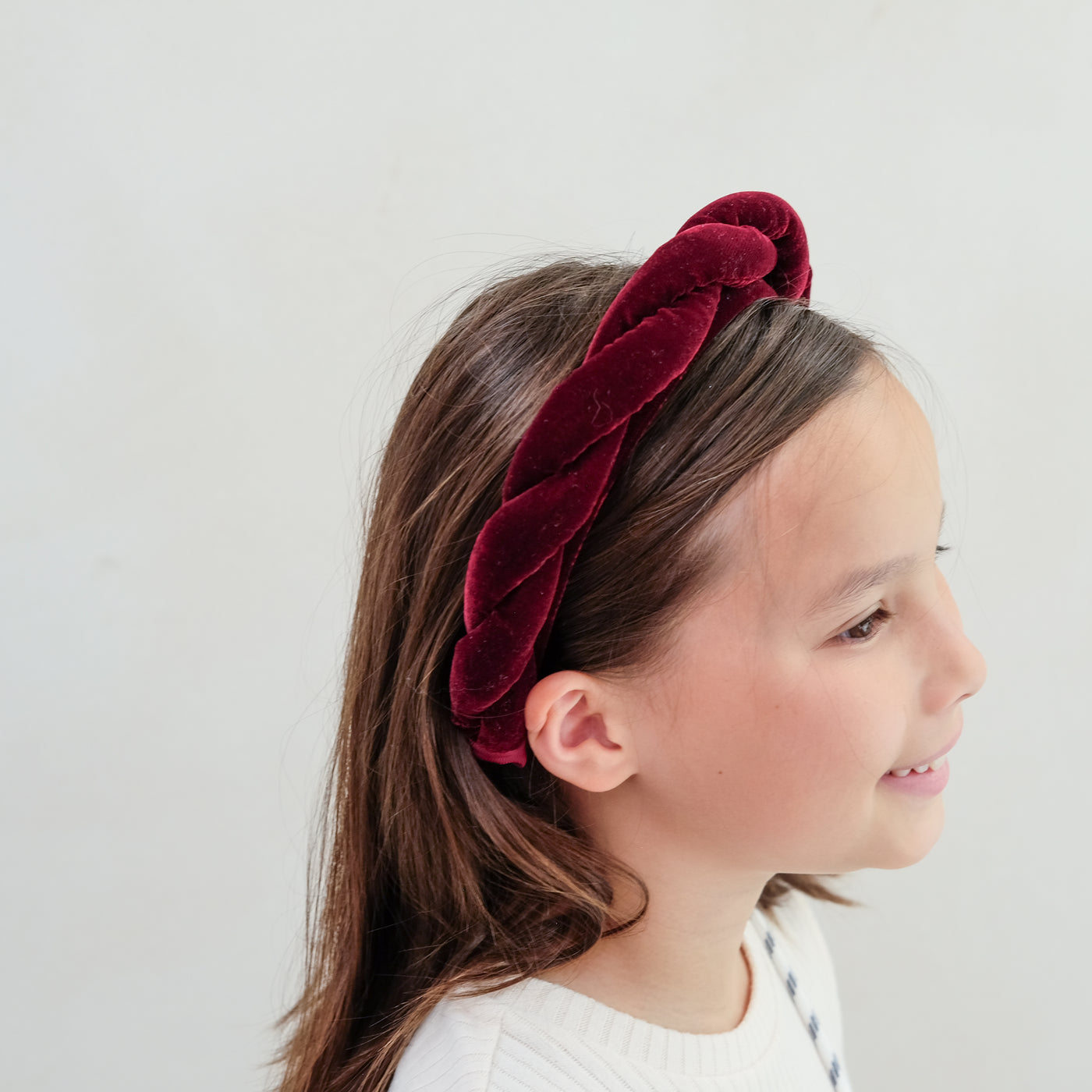 Young girl wearing a red velvet twist headband against a plain background