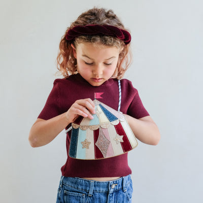 Child holding a colourful circus tent handbag with a plain background