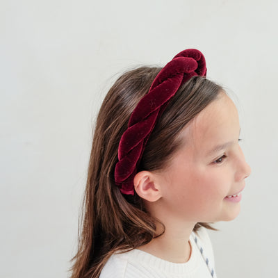 Young girl wearing a red velvet twist headband against a plain background
