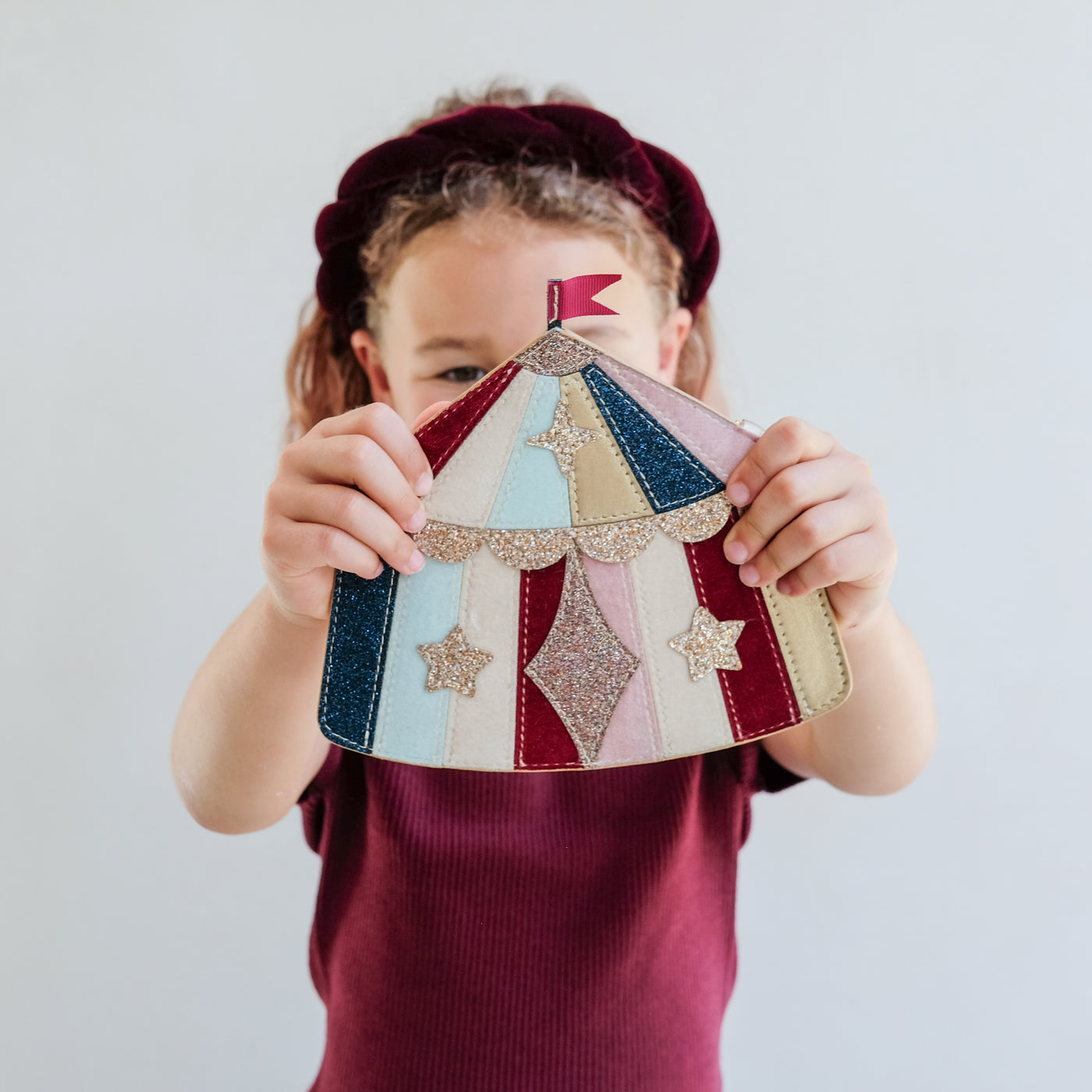 Child holding a colourful patchwork-style circus tent handbag with stars against a plain background