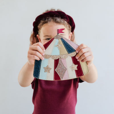 Child holding a colourful patchwork-style circus tent handbag with stars against a plain background