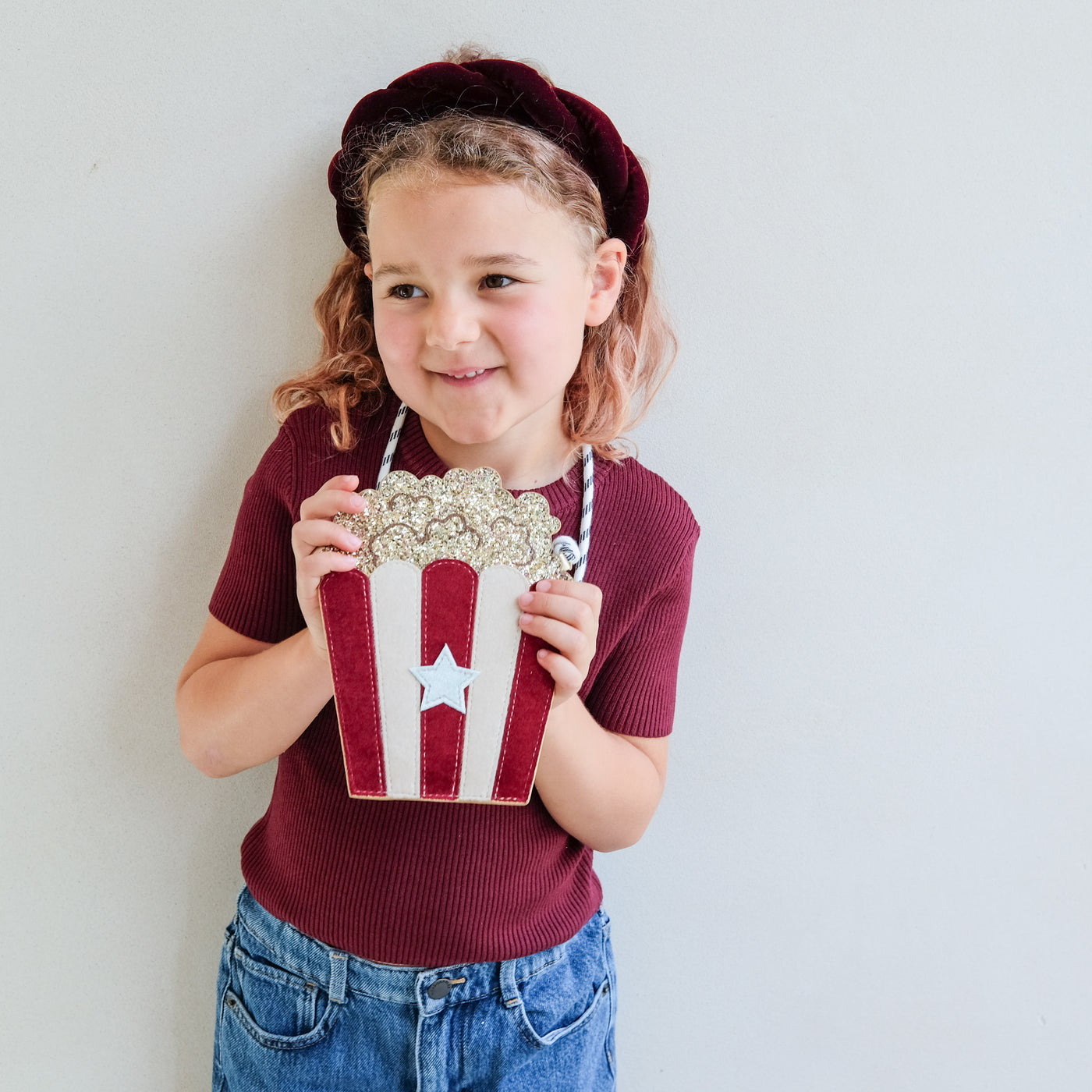 Child holding a decorative popcorn style bag against a plain background