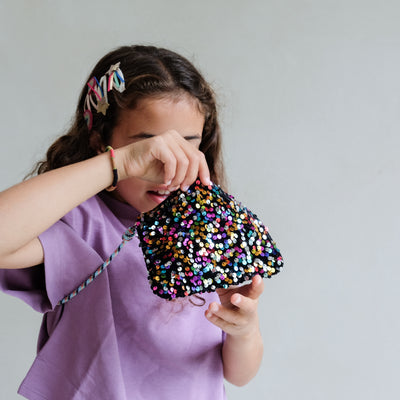 Child holding a colourful sequin bag against a plain background