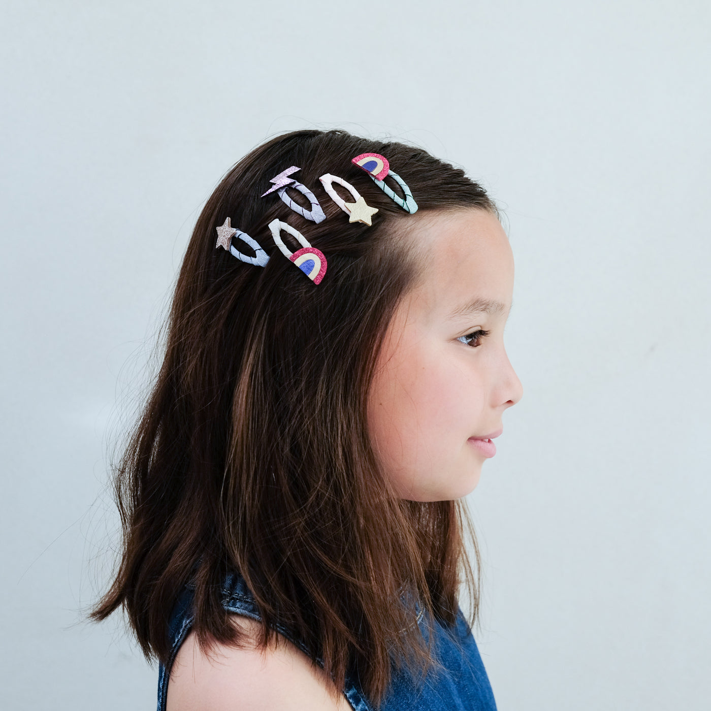 young girl wearing Rainbow mini clic clacs in her hair against a plain background