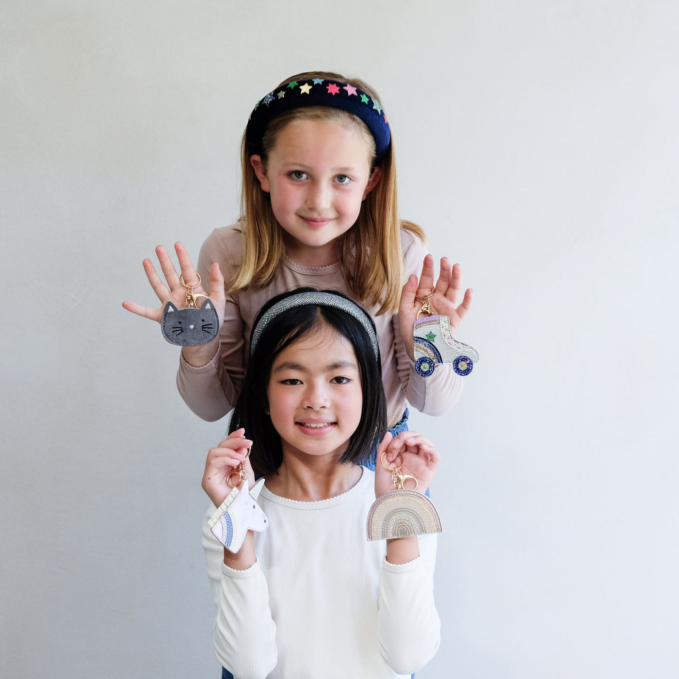 Two children holding colorful keychains against a plain background