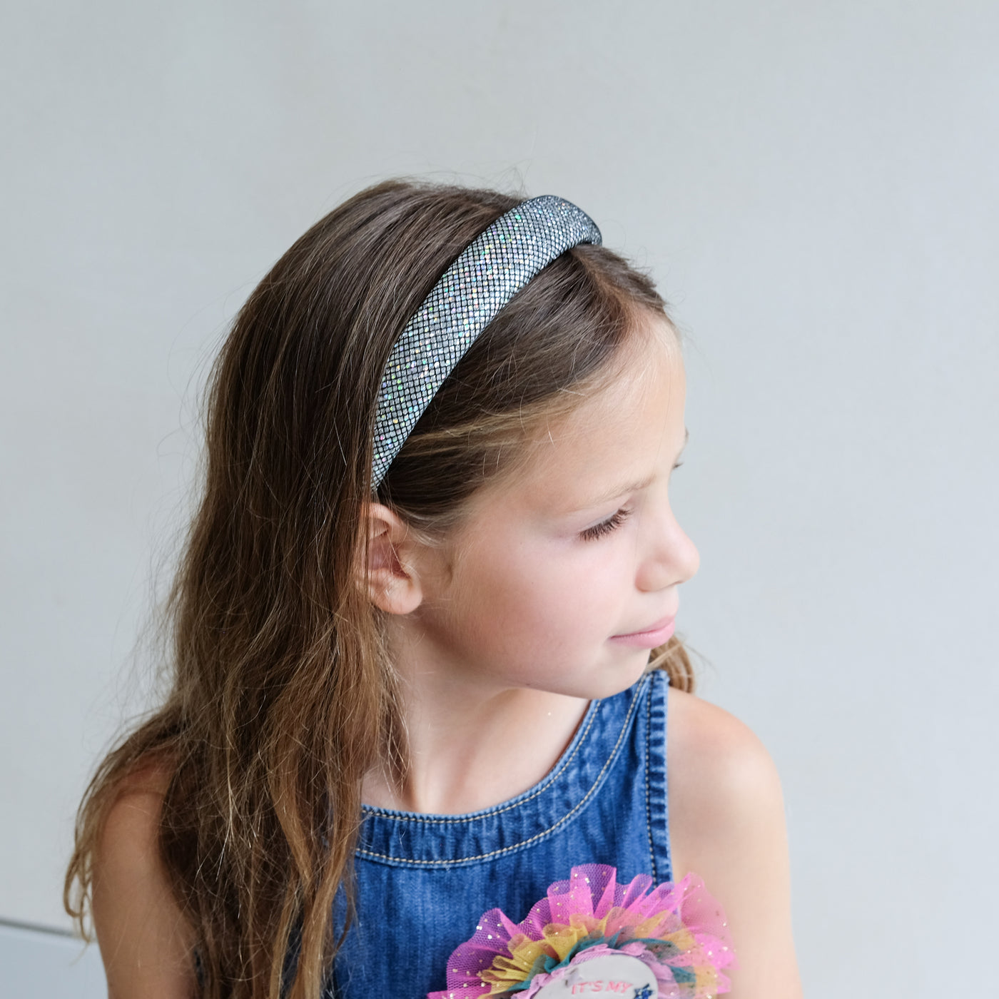 Young girl wearing a metallic silver padded headband with a plain background