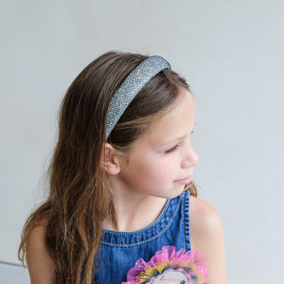 Young girl wearing a metallic silver padded headband with a plain background