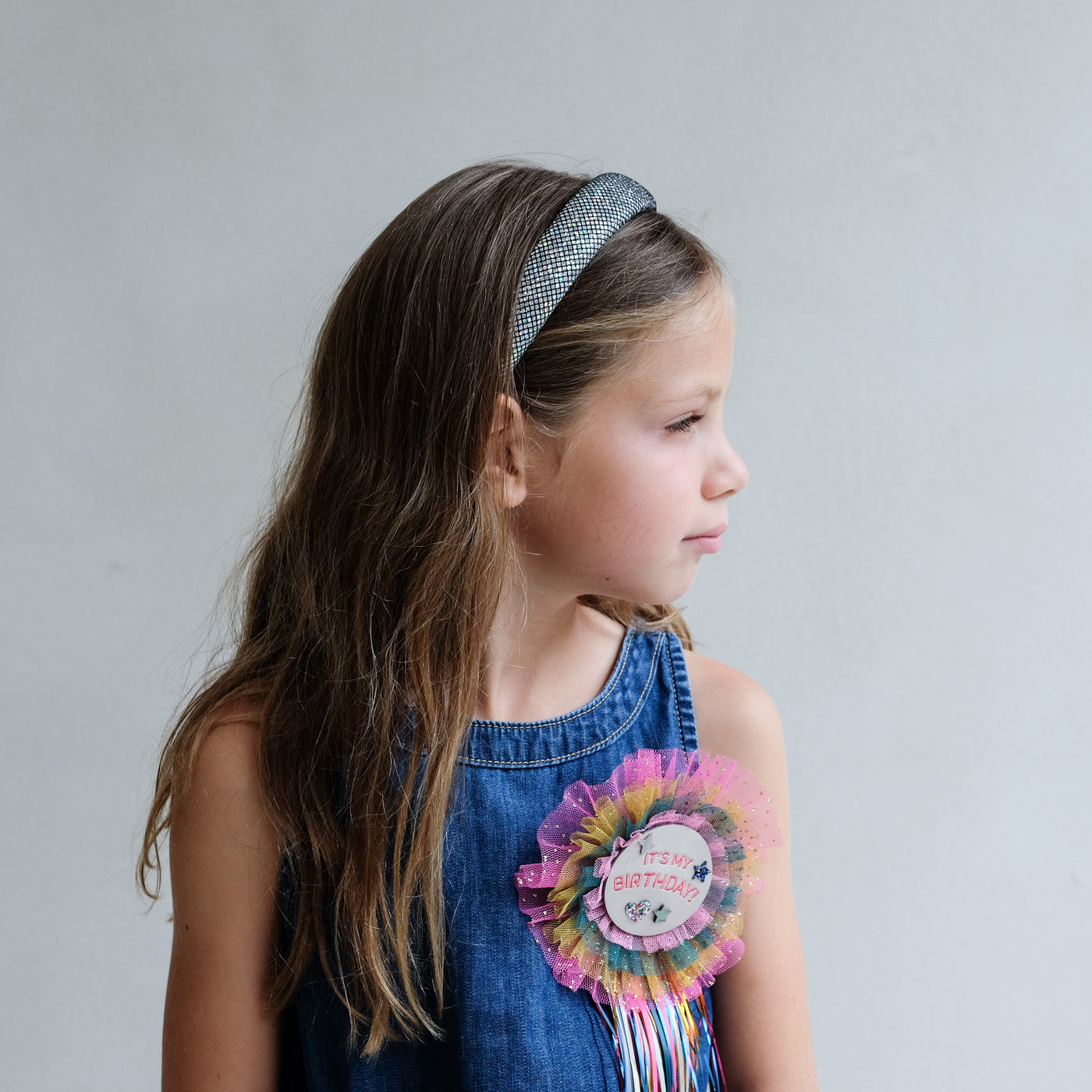 Young girl wearing a metallic silver padded alice band with a plain background