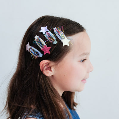girl wearing tinsel star clic clac hair clips in her hair against a white background