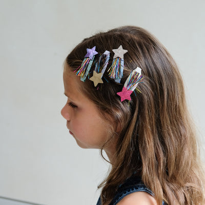 girl wearing tinsel star clic clac hair clips in her hair against a white background