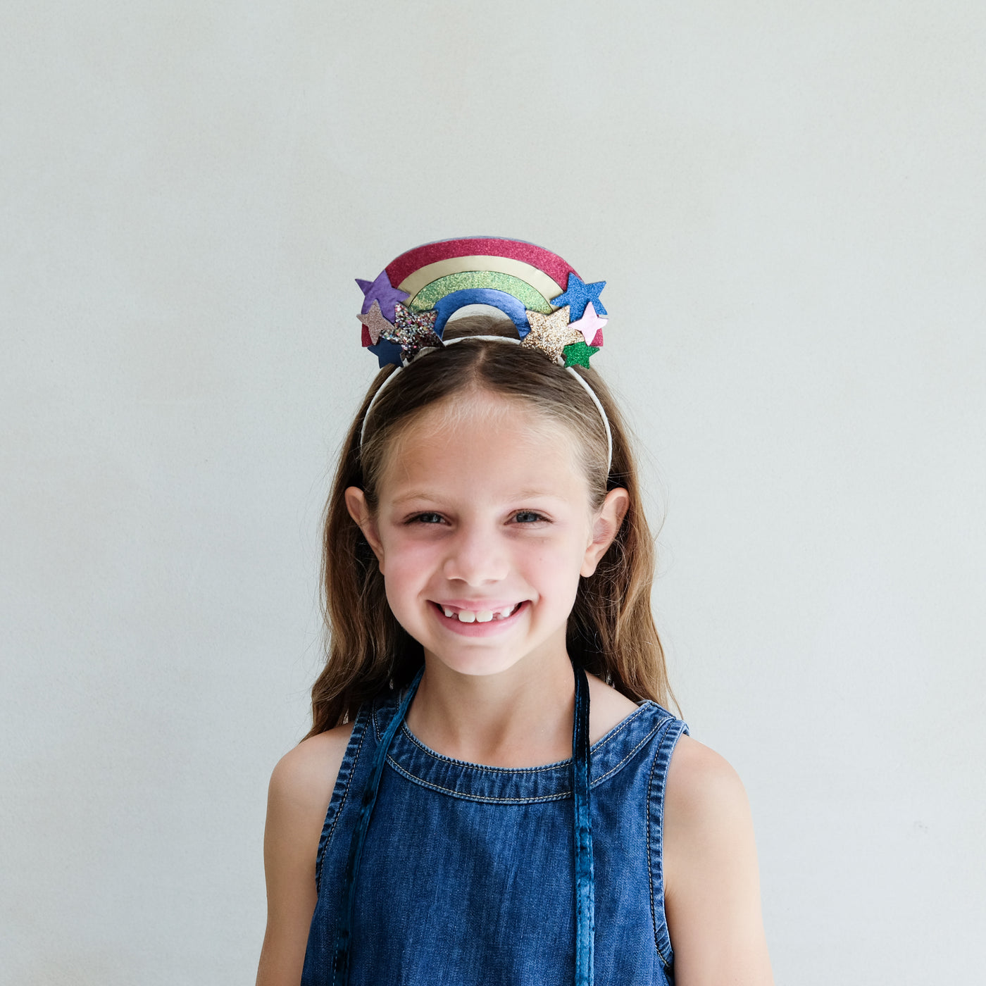 young girl wearing a rainbow headdress headband against a white background