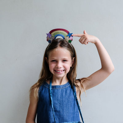 young girl wearing a rainbow headdress alice band against a white background