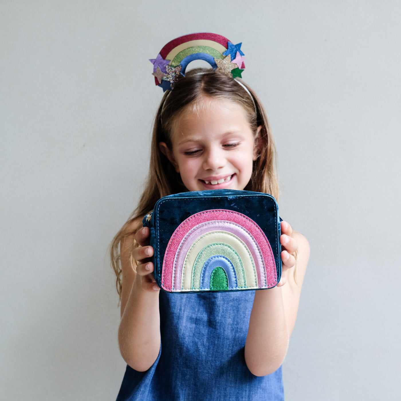young girl wearing a rainbow headdress headband holding a rainbow bag against a white background