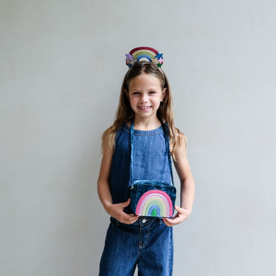Young girl holding a colourful rainbow bag with a plain background