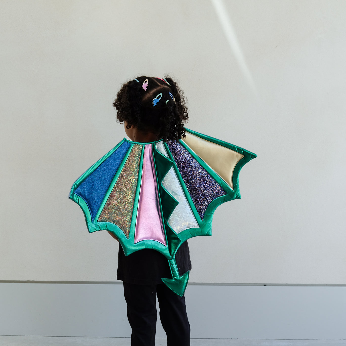 Child wearing a colourful dragon wings costume against a plain background