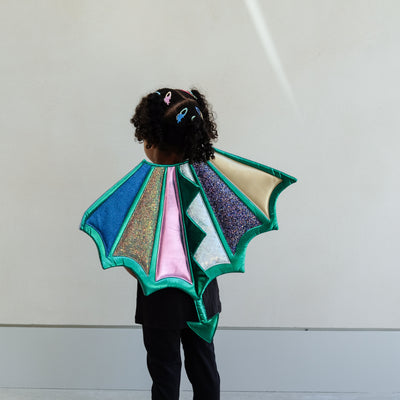 Child wearing a colourful dragon wings costume against a plain background