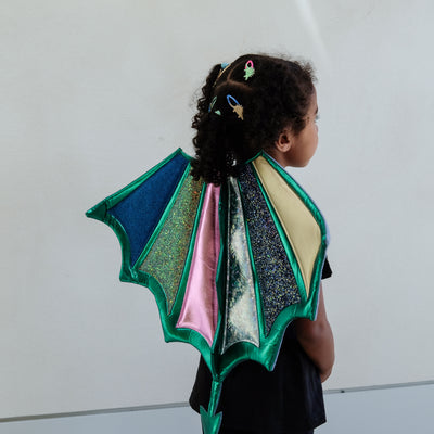 Child wearing a colourful dragon wings costume against a plain background