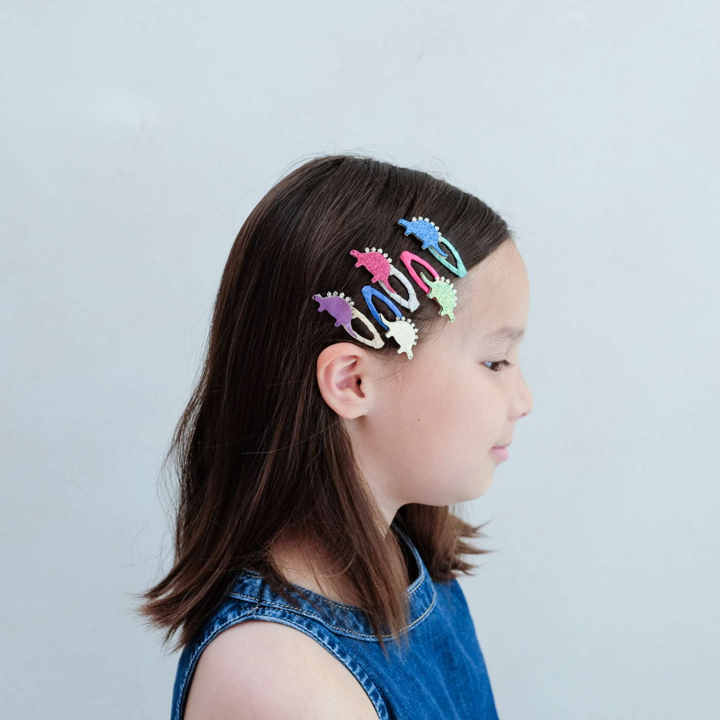 Child with colourful dinosaur hair clips in their hair against a plain background