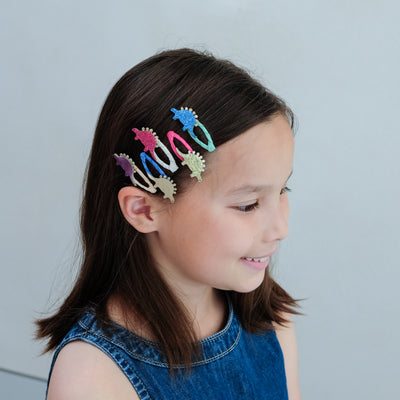 Girl with colourful dinosaur hair clips in her hair against a plain background
