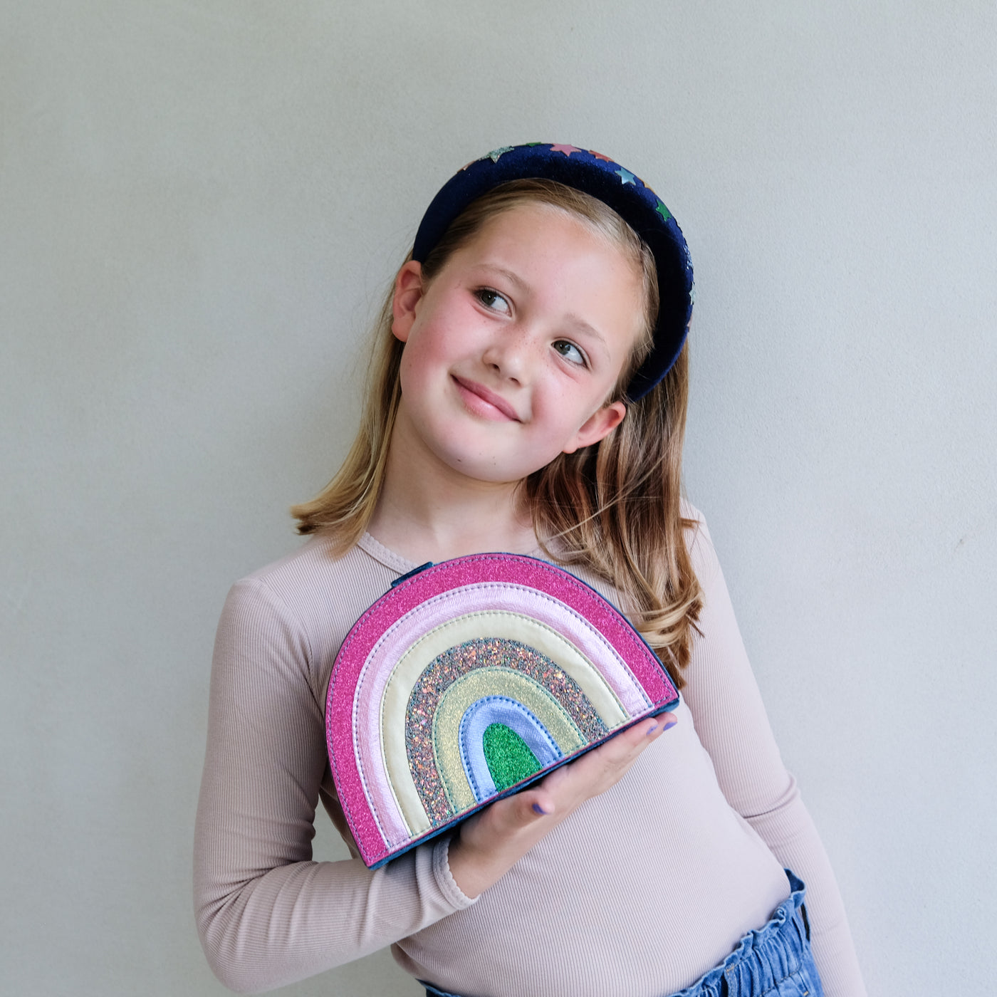 Young girl holding a colourful rainbow-shaped jewellery box against a plain background