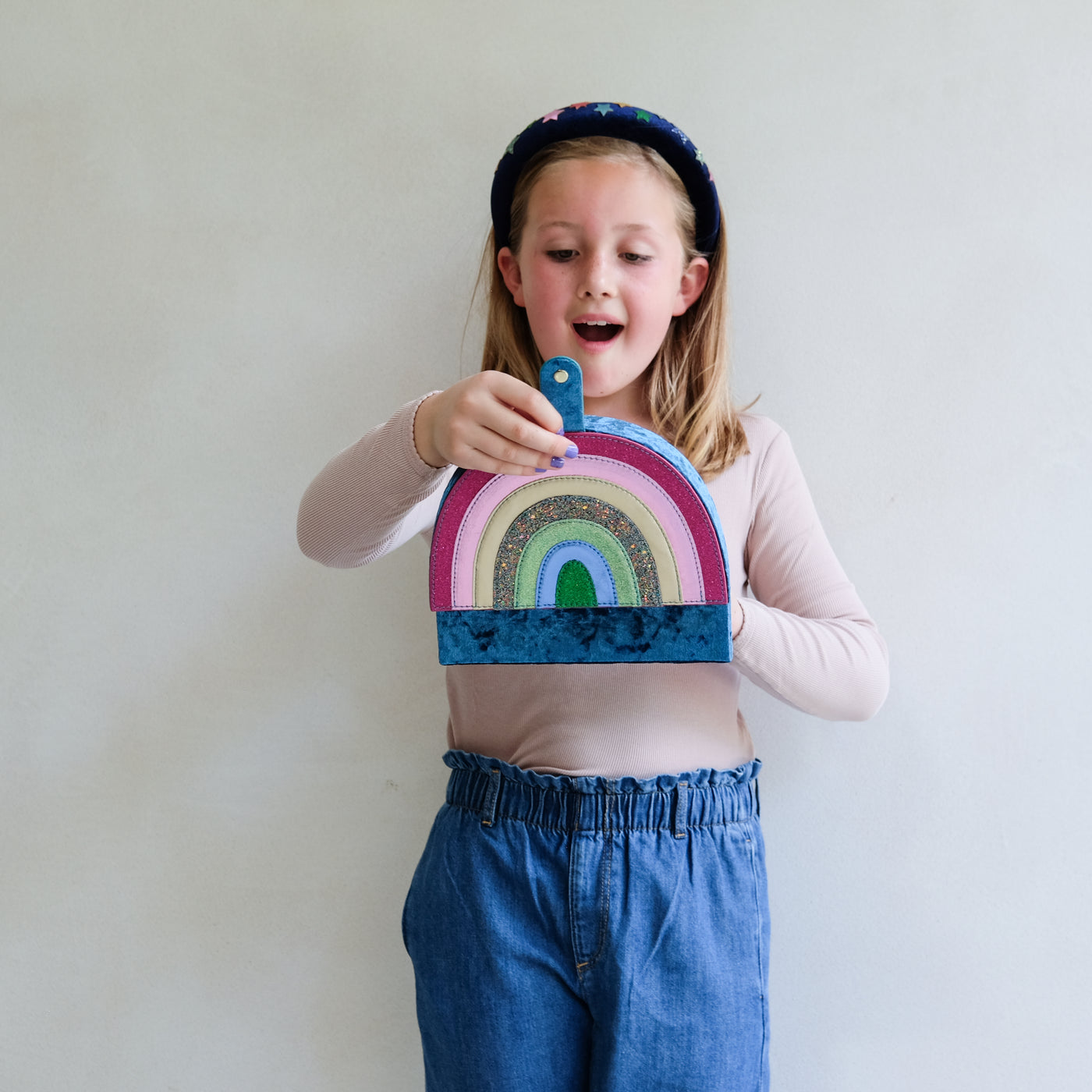 Child holding a colourful rainbow-shaped jewellery box against a plain background