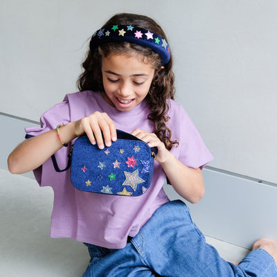 Girl wearing a night sky velvet cross body bag against a plain background