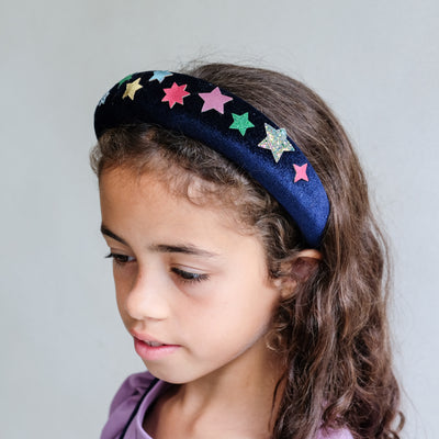 Young girl wearing a colourful star navy velvet headband against a plain background
