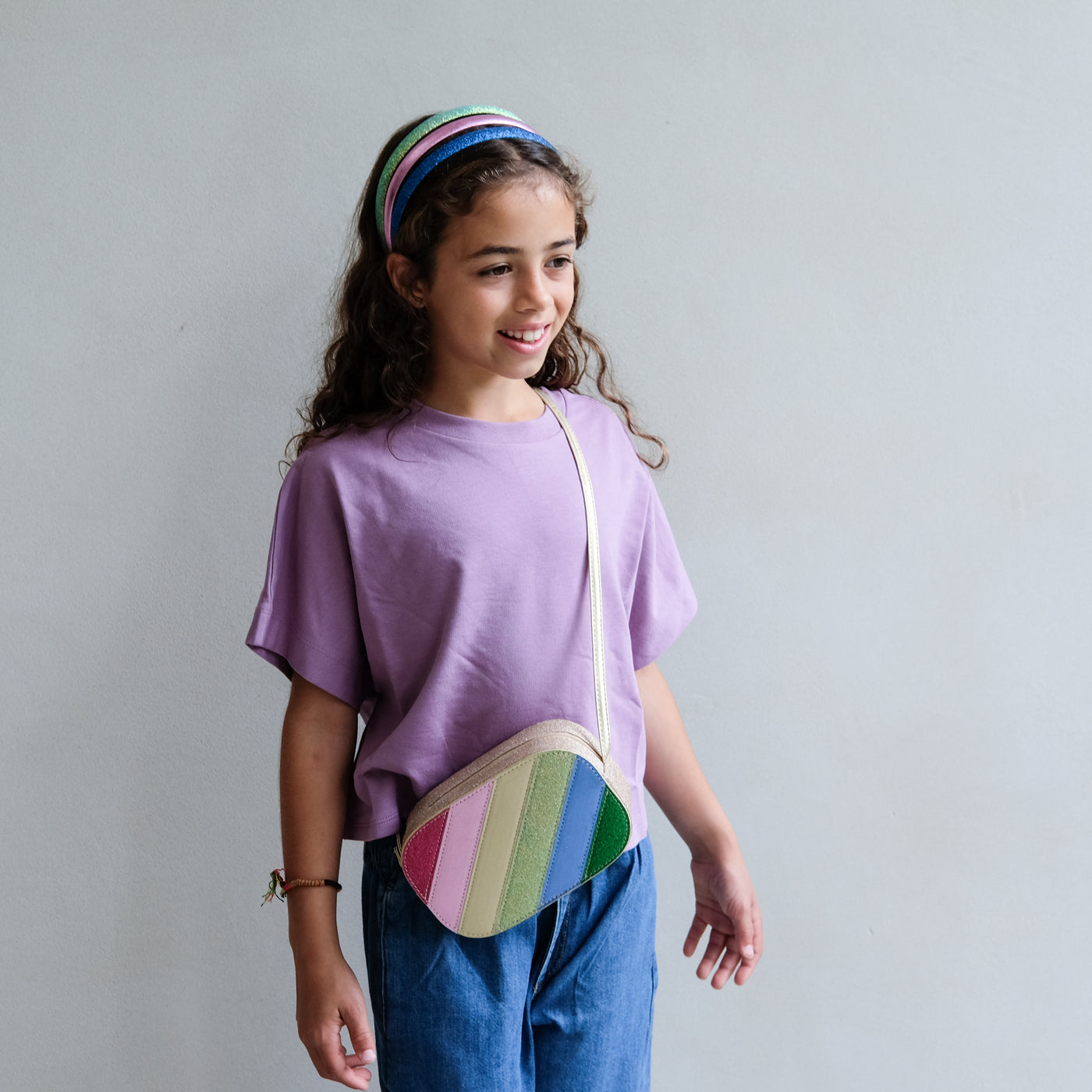 Girl wearing a colorful rainbow-patterned bag on a plain background