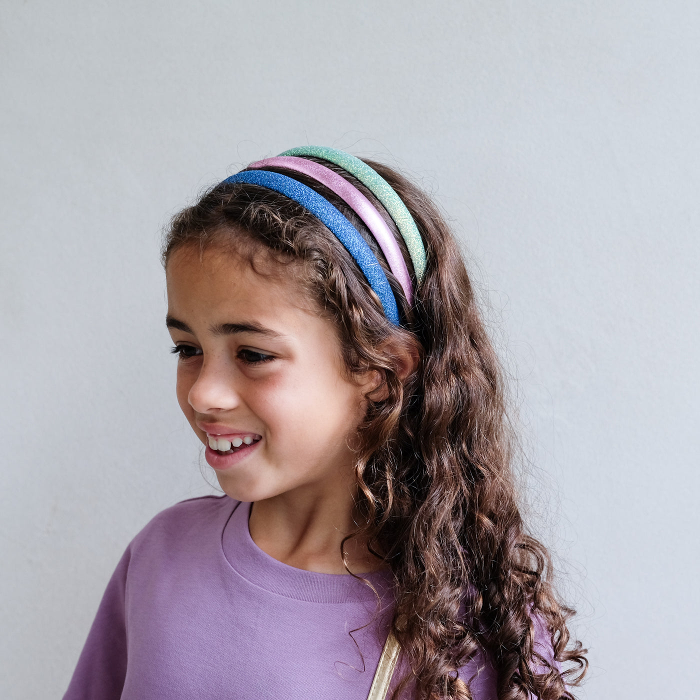 girl wearing a pack of iridescent medium alice bands against a white background