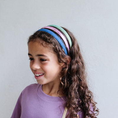 girl wearing a pack of iridescent medium alice bands against a white background