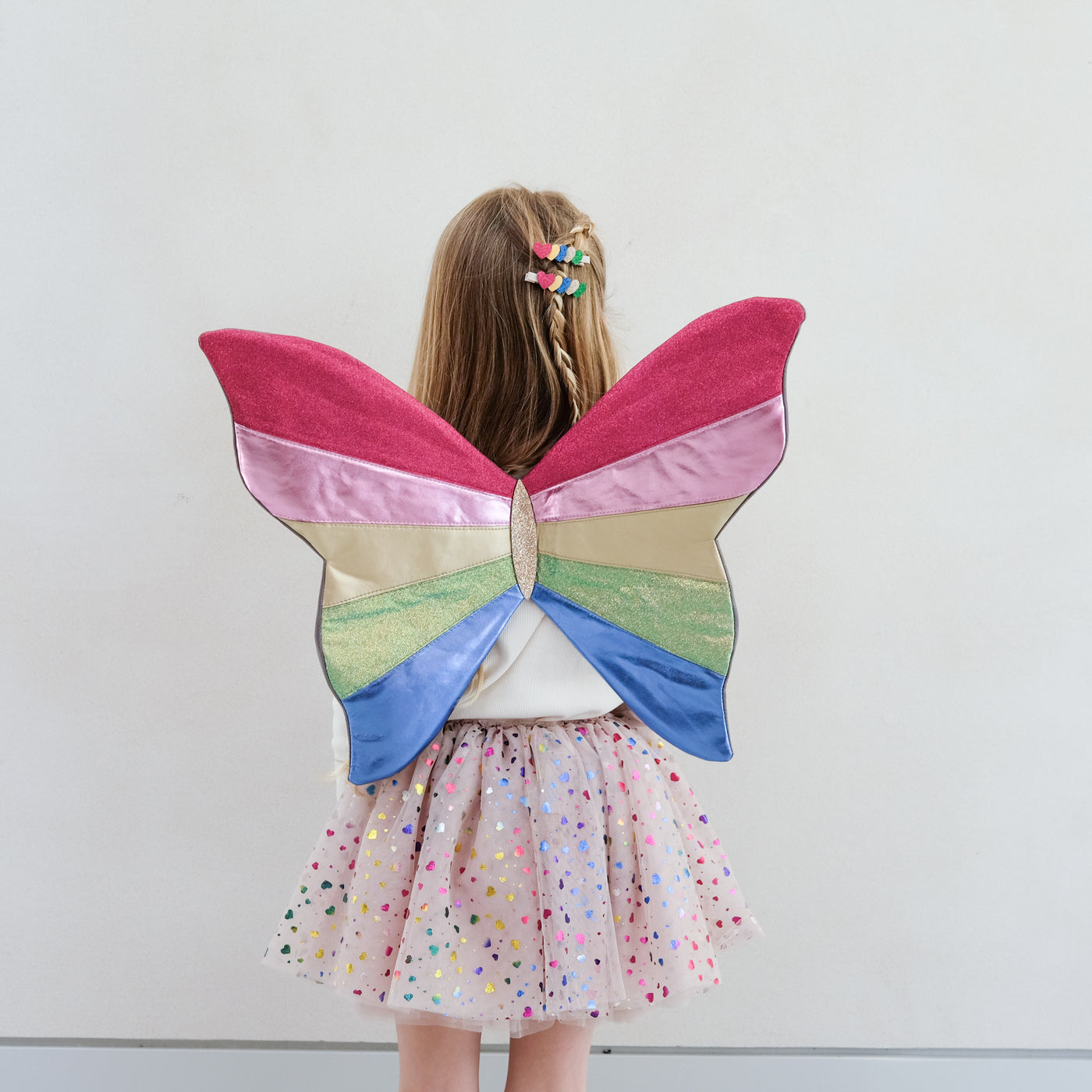 Child wearing colourful butterfly fairy wings against a plain background