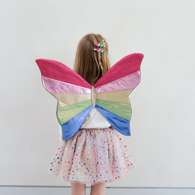 Child wearing colourful butterfly fairy wings against a plain background