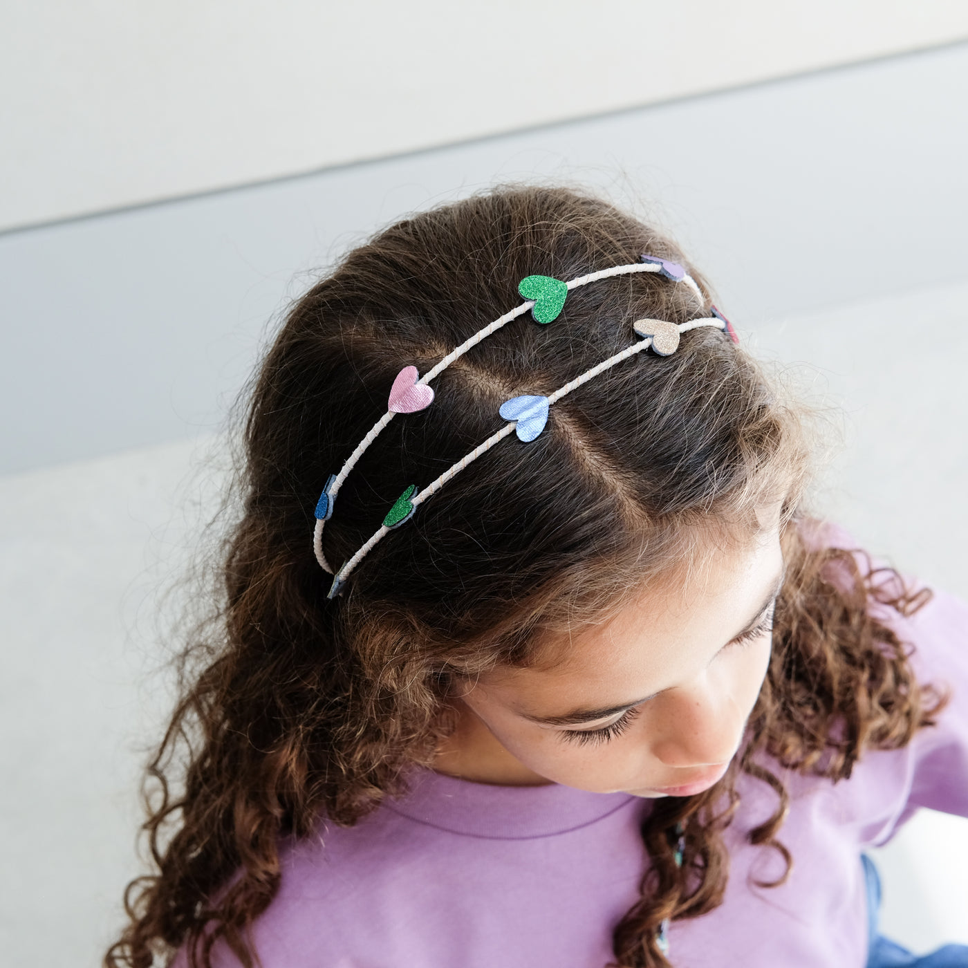 young girl wearing an rainbow heart headband against a white background