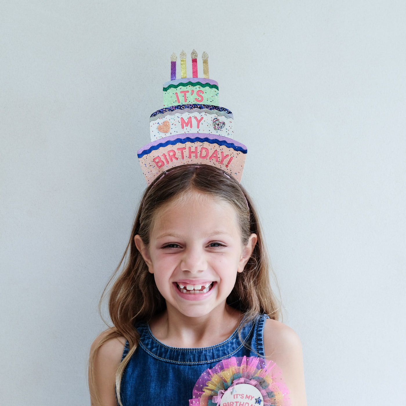 Young girl wearing a colourful birthday headdress against a light grey background