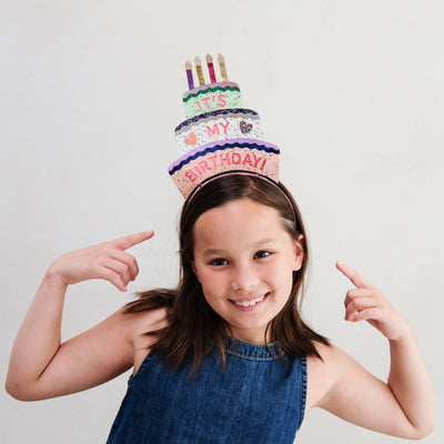 Young girl wearing a colourful birthday headband against a light grey background