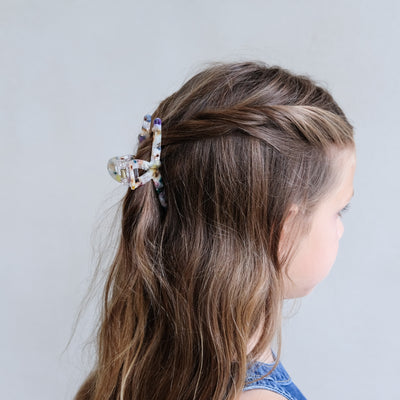 Girl with braided hair wearing a decorative hair clip against a plain background