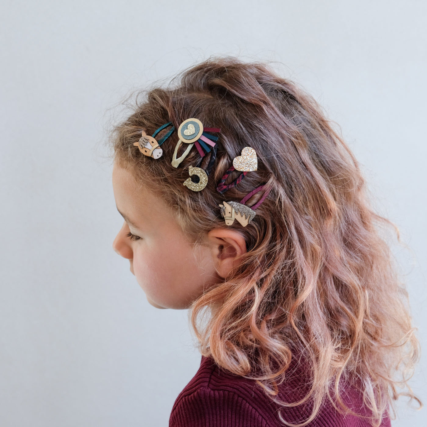 girl with curly hair wearing pony pals mini clic clac hair clips against a white background