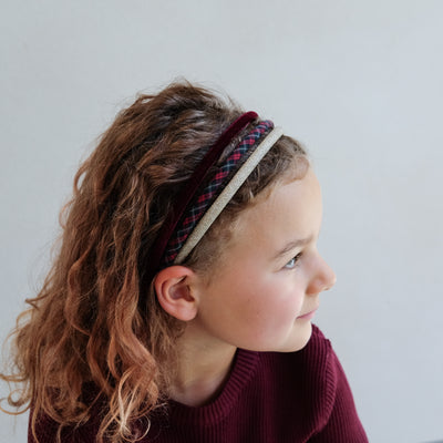 young girl wearing a pack of velvet, tartan, and gold glitter headband against a white background