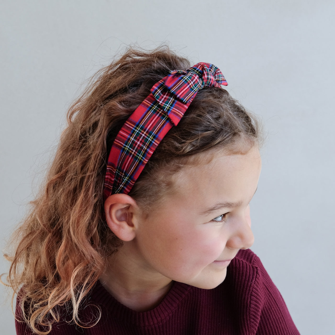 Child wearing a red plaid tartan headband against a plain background