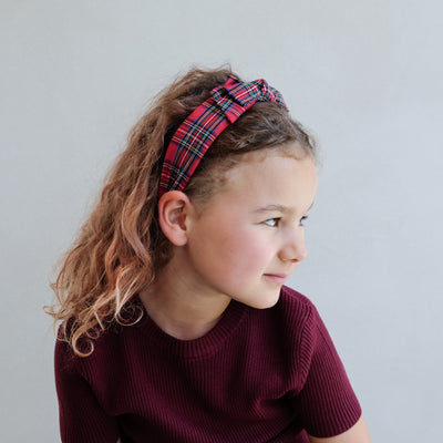 Young girl wearing a red tartan bow headband against a plain background