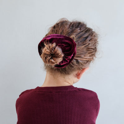 girl wearing giant red velvet scrunchie in hair against a white background