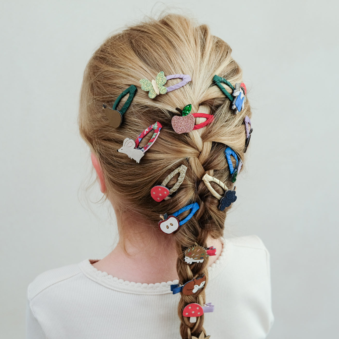 Child with braided hair adorned with various colourful girls hair clips on a plain background