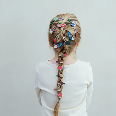 Child with braided hair adorned with colourful girls hair clips on a plain background