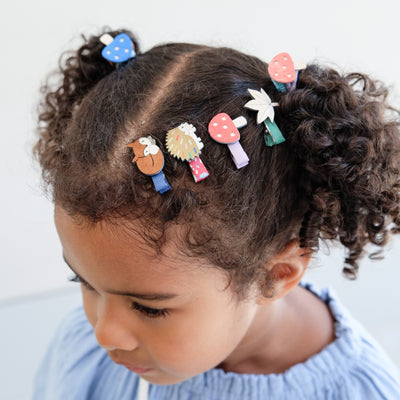 Child with colourful girls hair clips and hair ties in their hair against a light background