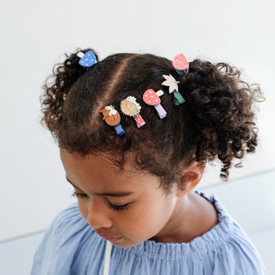 Child with colourful girls hair clips and hair bands in their hair against a light background