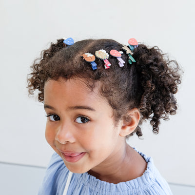 Child with curly hair adorned with colourful girls hair clips against a light background