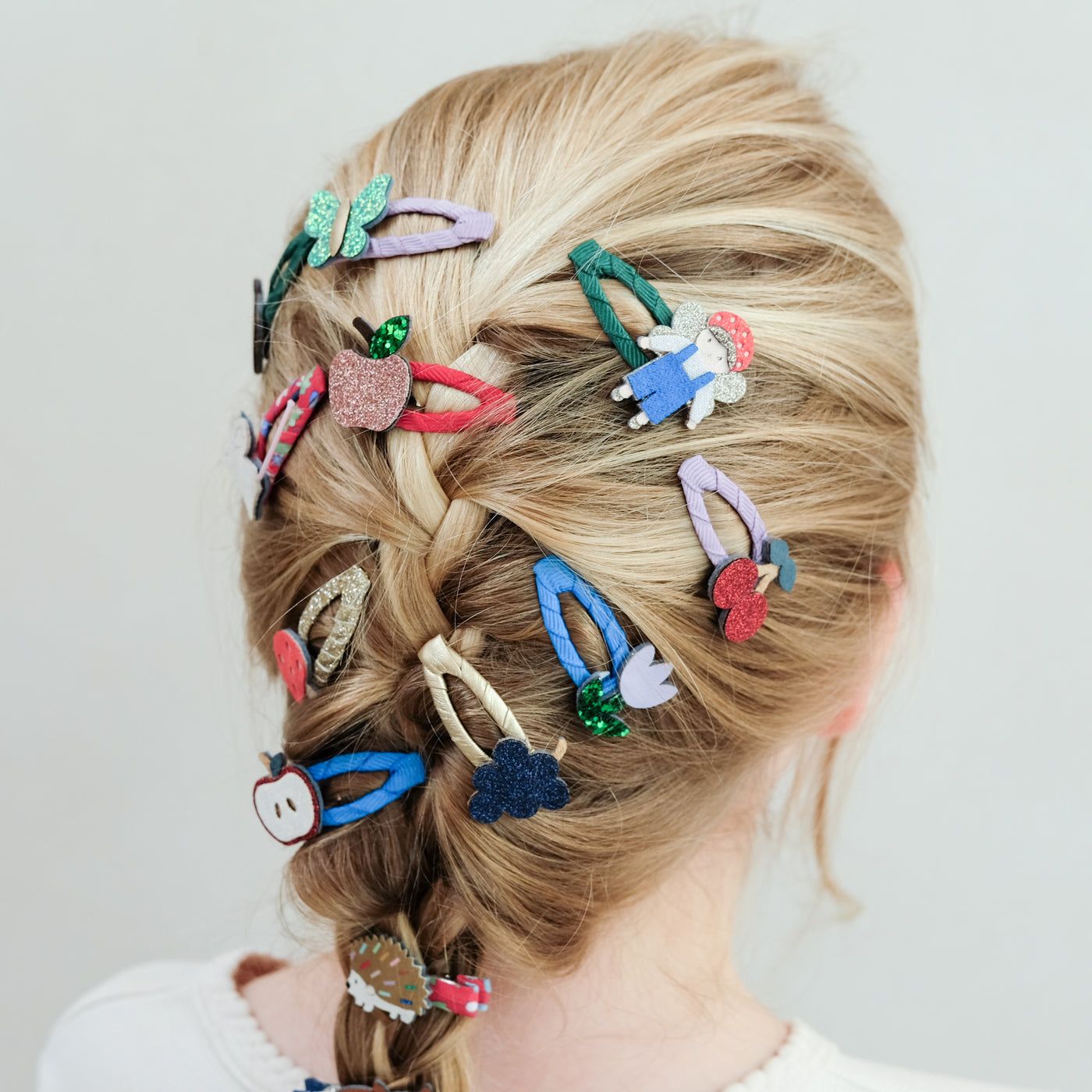 Colourful hair clips in a girl's braided hair against a white background