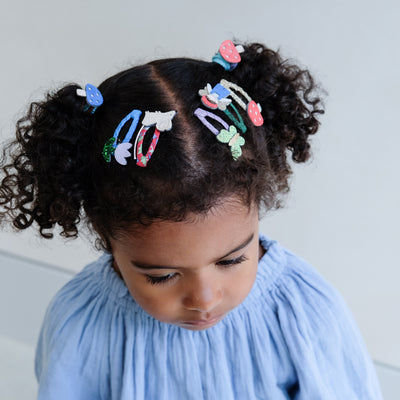 Child with curly hair wearing colourful girls hair clips and hair ties against a light background