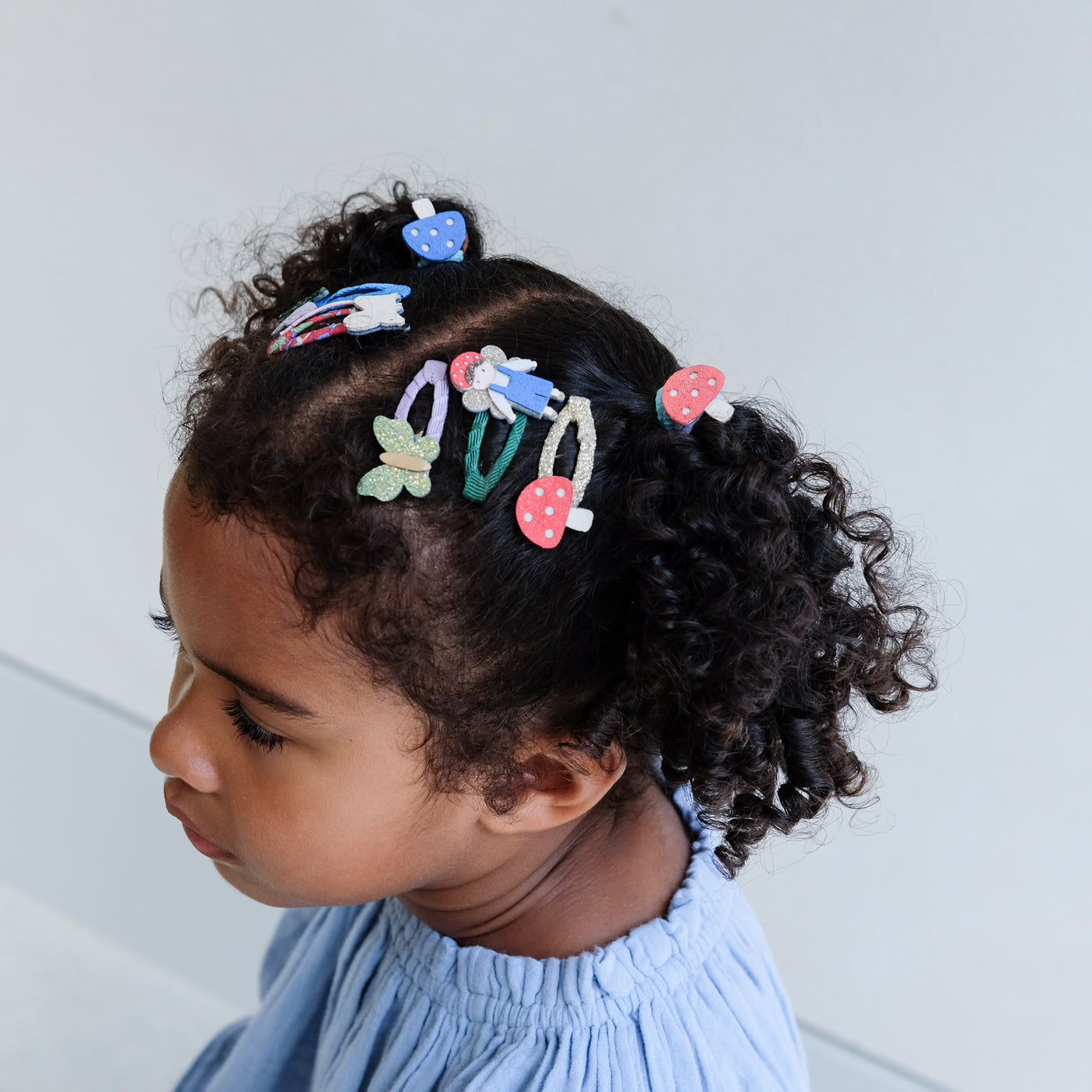 Child with colourful girls hair clips and hair bands in curly hair against a light background